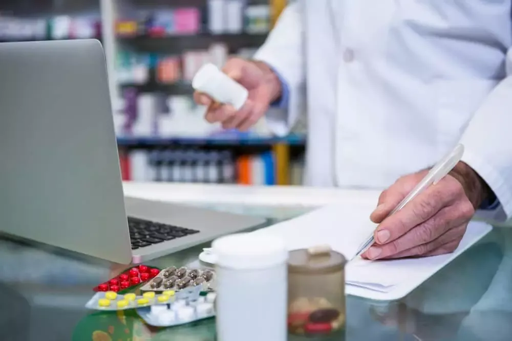 Pharmacien préparant une commande de médicaments devant un ordinateur portable