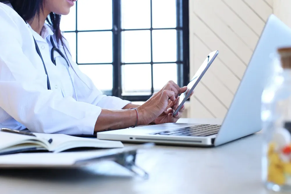 Médecin travaillant sur ordinateur portable et tablette dans son cabinet