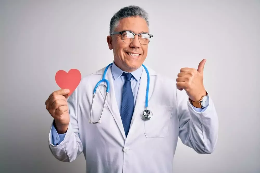Médecin souriant tenant un cœur en papier, pouce levé